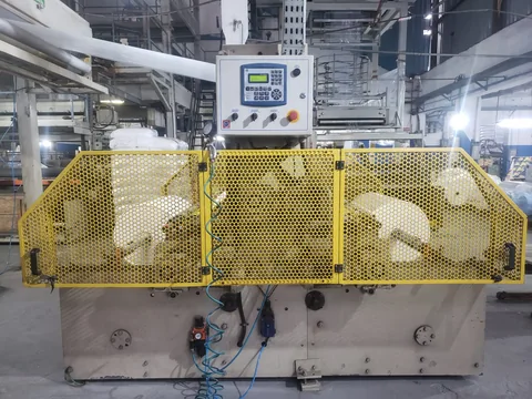 Máquina industrial com grades amarelas de proteção e painel de comando.